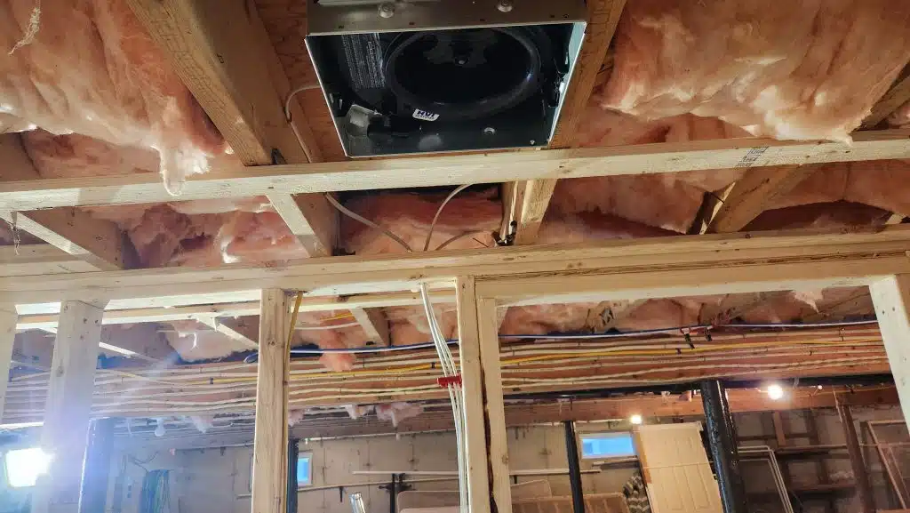 Bathroom exhaust fan housing installed between basement ceiling joists
