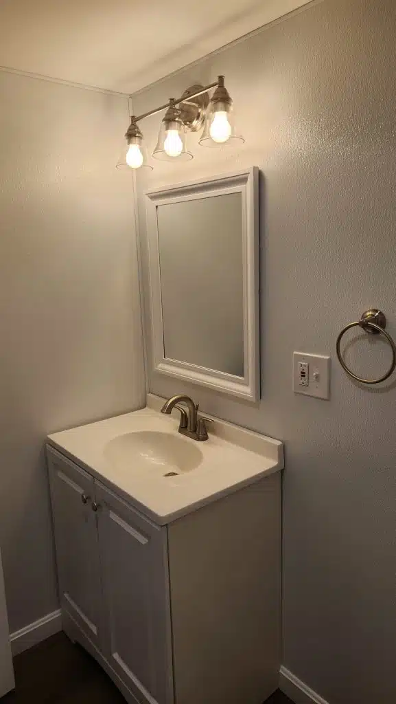 Finished basement bathroom vanity with three-light bar and GFCI outlet