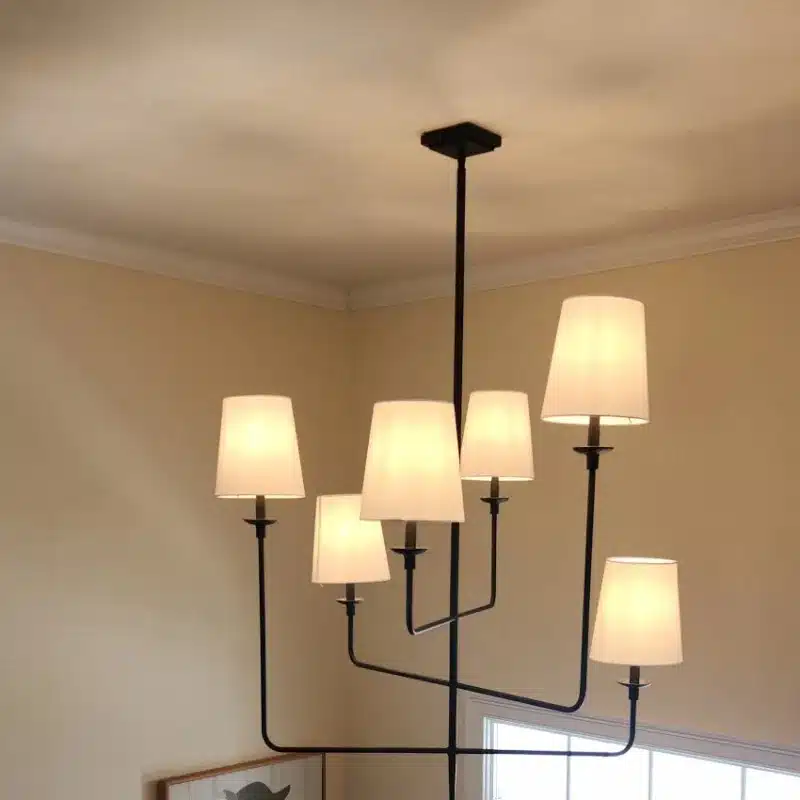 Six-light chandelier with white shades installed in a two-story entryway